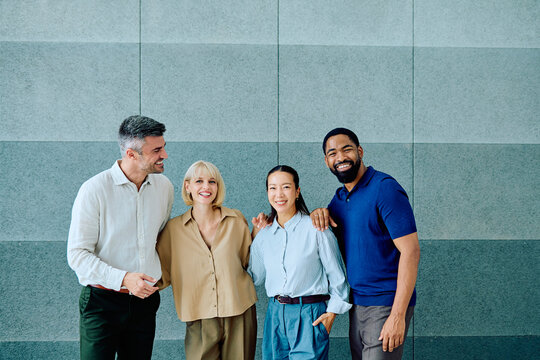 Diverse group of four standing together, smiling and embracing, showcasing unity and successful partnership in a modern office