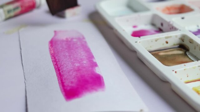 Artist painting with watercolor on paper using water to create soft texture and color effects. Close up of paintbrush blending wet paint in home studio during creative painting process.