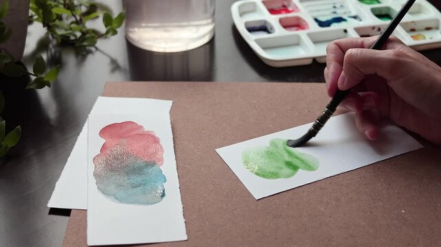 Artist painting with watercolor on paper using water to create soft texture and color effects. Close up of paintbrush blending wet paint in home studio during creative painting process.
