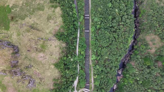 Aerial drone push forward top down shot of water pipes running down the mountain to the village Kinlochleven at the Loch Leven, part of the West Highland Way in Scotland.