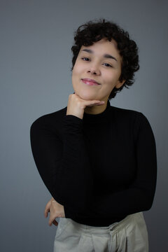 Lovely young woman smiling and posing with chin on hand. Waist up studio portrait with copy space, ideal for gen z, femininity, positive emotion, and young adulthood themes.