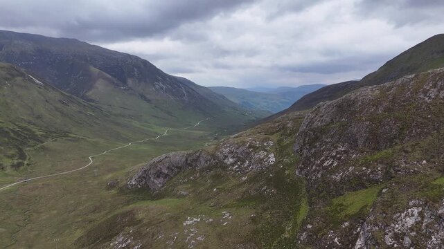 Aerial drone push forward shot of a large valley with a winding road on the West Highland Way in Scotland.