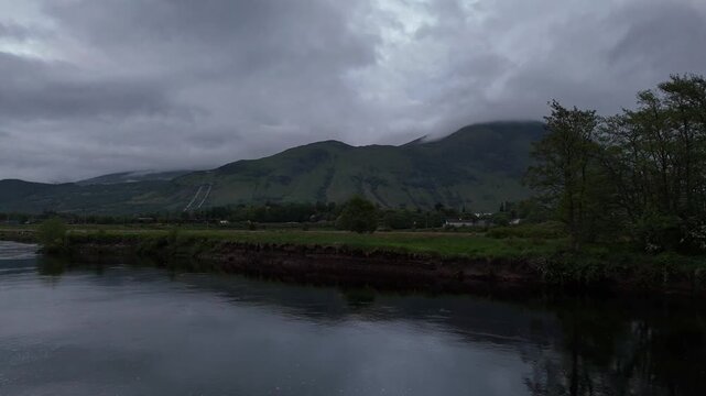 Aerial drone push forward shot of Ben Nevis in Scotland. Shot from the town Fort William over a lake with surrounding trees at night.