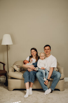 A family portrait of parents with a newborn baby and an older daughter on the sofa.