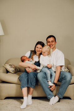 A family portrait of parents with a newborn baby and an older daughter on the sofa.