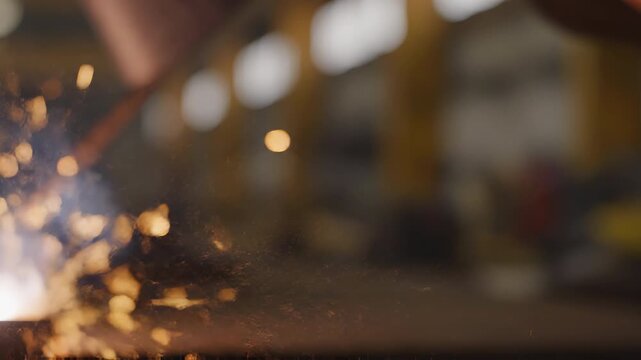 Close-up of bright welding sparks flying during metalwork in an industrial workshop with a blurred bokeh background.