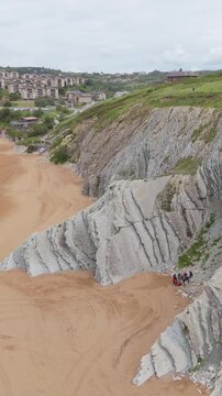 Aerial view of striped flysch cliffs with people on secluded beach, Basque Country