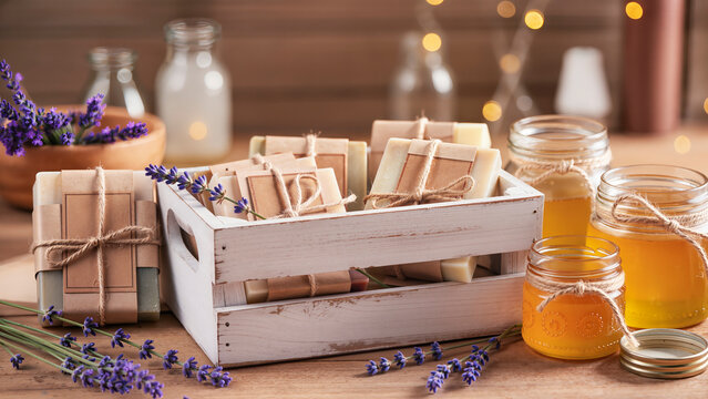 Handmade craft soap bars packaged with twine in wooden crate next to honey jars and fresh lavender flowers on rustic table