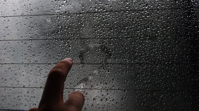 Close-up of a person drawing a heart on a foggy, rain-covered car window. Moody scene symbolizing love, romance, connection, and rainy travel.
