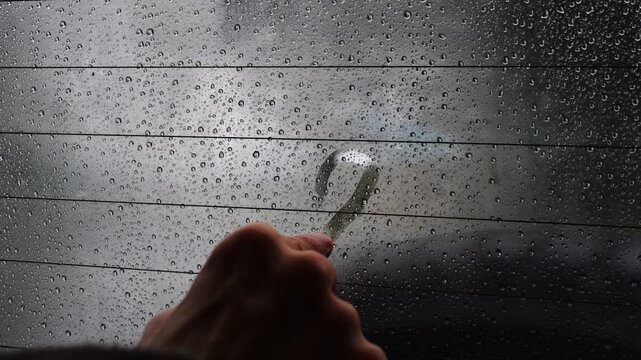 Person slowly draws a heart shape on a foggy, rain-covered car window. Creative, moody, and contemplative moment symbolizing love and connection on a rainy journey.