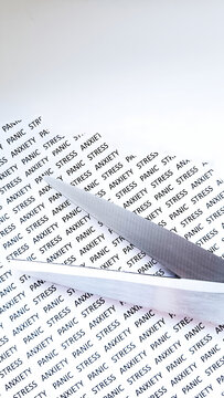 Cutting away stress and anxiety. Metal scissors blade divides a paper covered in repeating text "STRESS" and "ANXIETY". Mental health metaphor.