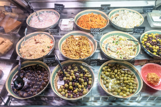 Large amount of choices within a deli store including pastas, coleslaw, olives and potato salad. Seen in a chiller unit.