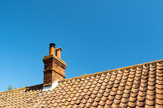Detailed view of a clay tile roof and brick built chimney seen on a typical cottage roof in Britain. Seen against a clear blue coastal sky in summer.