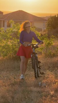 Young woman with bicycle at sunset on a scenic hillside. Slow zoom shot.