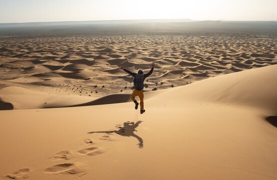 Young man walking down a sand dune, dune landscape Erg Chebbi, Merzouga, Sahara, Morocco