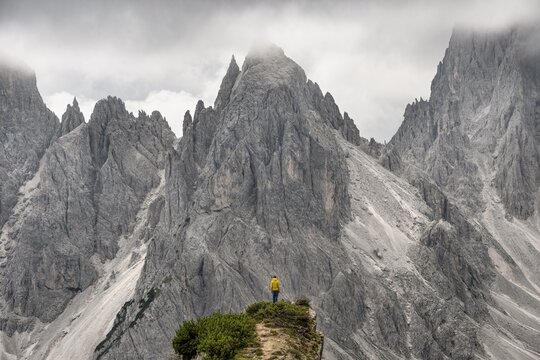 Hiker standing on a ridge, mountain peaks and pointed rocks behind, dramatic cloudy sky, Cimon di Croda Liscia and Cadini group, Auronzo di Cadore, Belluno, Italy