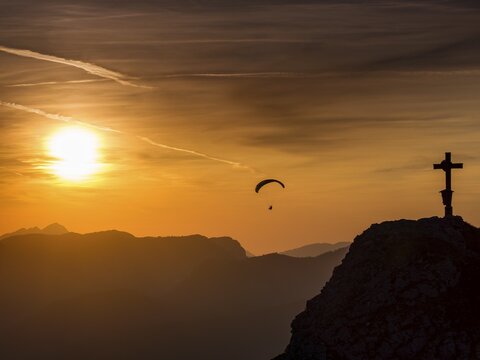 Paraglider flying next to the summit cross of the small Jenner at sunset, Reiteralpe in the background, Berchtesgaden National Park, Sch&ouml;nau am K&ouml;nigssee, Upper Bavaria, Bavaria, Germany