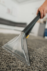 Carpet cleaning extractor nozzle lifting dirt from gray carpet in bright indoor room with handheld tool, visible grip, clear suction chamber, damp fibers, and fresh cleaned surface © Anastasia
