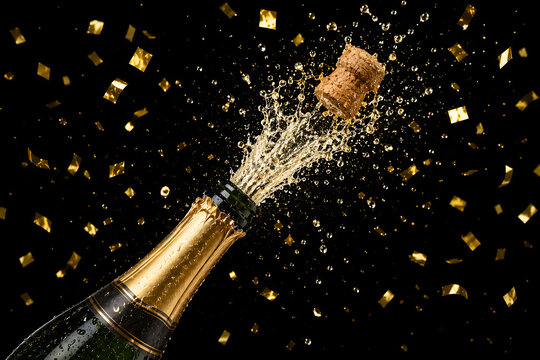Champagne bottle popping cork with explosion of golden confetti on black backdrop.