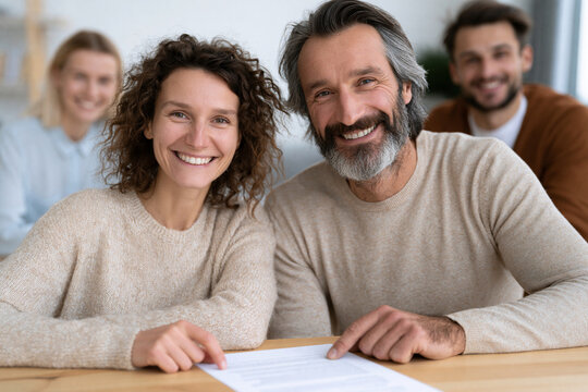 Warm smiles fill this friendly, collaborative scene. Two people sit together, hands resting on a document. Their joyful expressions suggest mutual trust and satisfaction. The setting implies teamwork