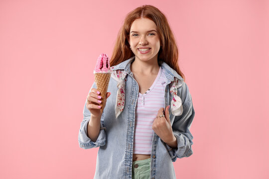 Happy teenage girl with delicious ice cream in waffle cone on pink background