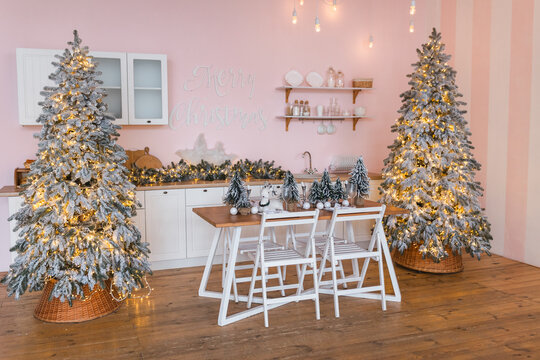 Spacious pink kitchen interior decorated for Christmas with two illuminated frosted pine trees.