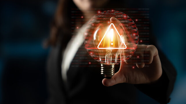 A business professional holds a glowing light bulb featuring a warning symbol, symbolizing the importance of understanding technology risks and data security threats. Gantry