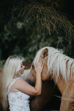 Blonde woman with horses in the garden in summer