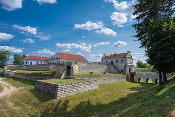 Fototapeta premium the expansive grounds and architectural grandeur of Zbarazh Castle, showcasing its fortified walls, gatehouse, and scenic moat area under a sunny sky.
