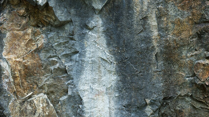 Fototapeta premium High resolution close up photograph of a natural rough rock wall surface showcasing detailed stone textures, organic crack patterns, weathered mineral layers, and rugged mountain geological formations