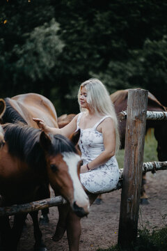 A blonde woman walks with horses in the forest