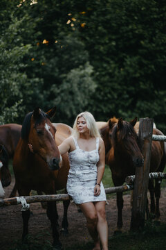 A blonde woman walks with horses in the forest