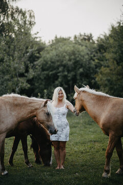 A blonde woman walks with horses in the garden in summer