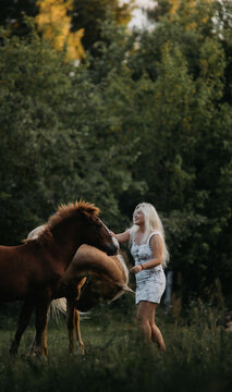 A blonde woman walks with horses in the garden in summer