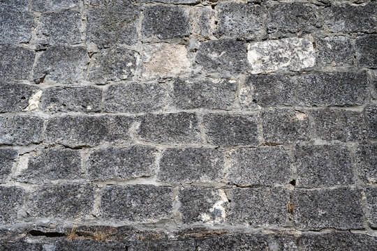 a weathered, dark grey stone wall featuring roughly hewn rectangular blocks and light grey mortar.
