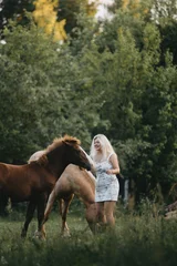 A blonde woman walks with horses in the garden in summer © velimir