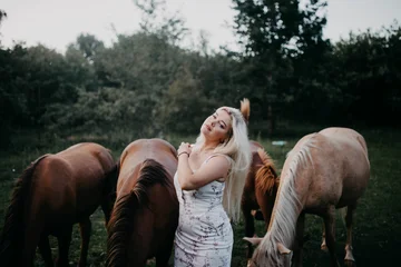 A blonde woman walks with horses in the garden in summer © velimir