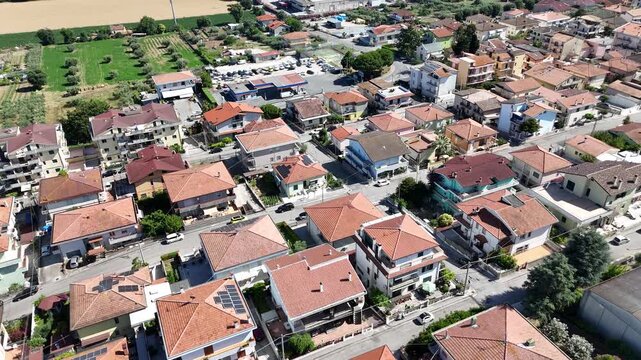 High angle drone view of Roseto degli Abruzzi town rooftops and residential houses surrounded by green hills under blue sky in Abruzzo region Italy.