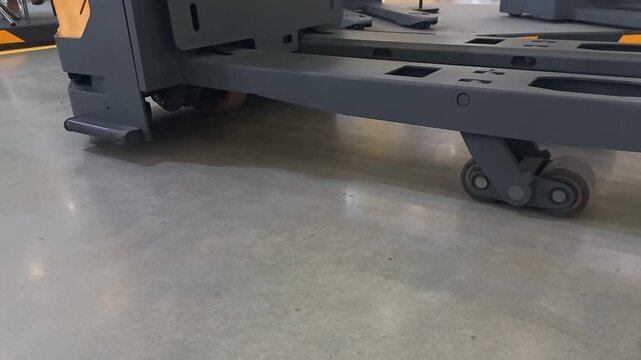 Industrial electric pallet jack load wheels and metal forks mechanism base structure detail on concrete floor background inside automated logistics warehouse facility material handling equipment