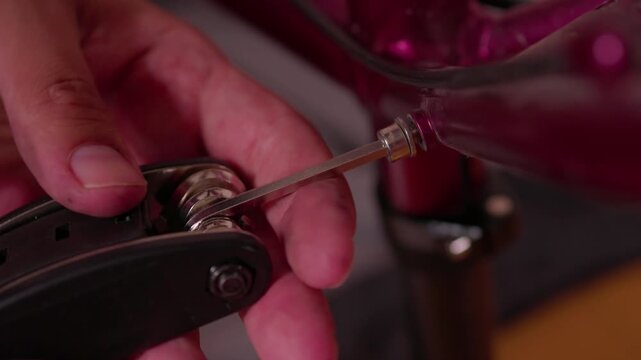 hands adjusting bicycle seat post clamp in indoor workshop setting with red and black components focused and practical close-up perspective on metallic and plastic materials.
