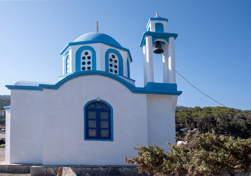 White and blue Greek Orthodox chapel by the sea in Ikaria island under blue summer sky, Greece
