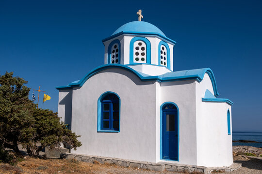 White and blue Greek Orthodox chapel by the sea in Ikaria island under blue summer sky, Greece