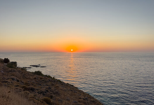 Pastel sunset over calm Aegean Sea and rocky shore at Cavos Bay on Ikaria Island Greece
