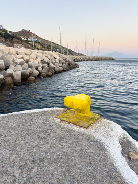 Yellow mooring bollard beside calm Aegean harbor at dusk in Agios Kirikos, Ikaria island, Greece