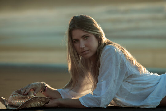 Woman with straw hat relaxing on beach at sunset