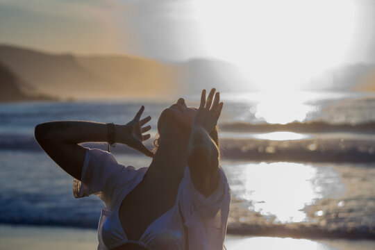 Woman enjoying ocean sunset with arms raised