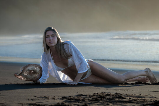 Young woman relaxing on black sand beach at sunset