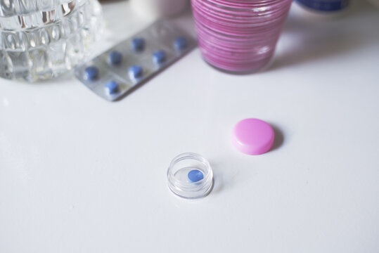 Pastilla azul en contenedor o pastillaro con tapa rosa sobre mesa junto a un vaso rosa y un blister con pastillas azules