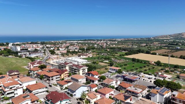 High angle drone view of Roseto degli Abruzzi town rooftops and residential houses surrounded by green hills under blue sky in Abruzzo region Italy