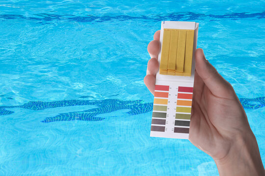 Man with pH test strips and color table by swimming pool, closeup